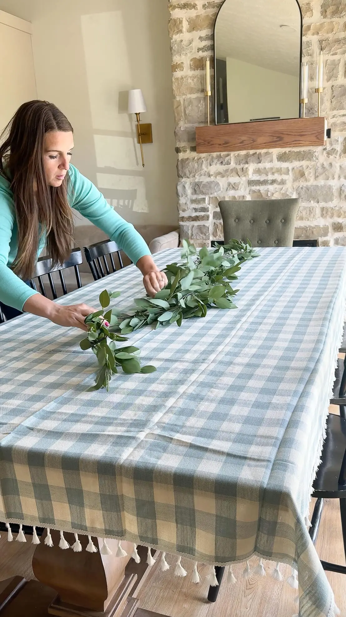 Woman arranging a eucalyptus garland on a gingham tablecloth during the early stages of spring table decorating.